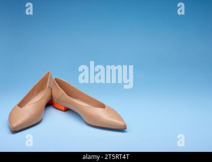 A pair of modern beige pointed-toe ballet shoes. Contrast design with bright orange heels. Isolated on a gradient blue background with large copy spac Stock Photo