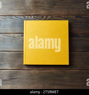 Yellow hardcover photobook isolated on a wooden background with copy space. Top view, flat lay. Blank closed book mockup for placing custom text or im Stock Photo