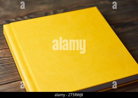 Photo album with bright yellow hardcover isolated on a brown wooden background. Perspective view, close-up. Printing photos from photoshoots. Layout w Stock Photo