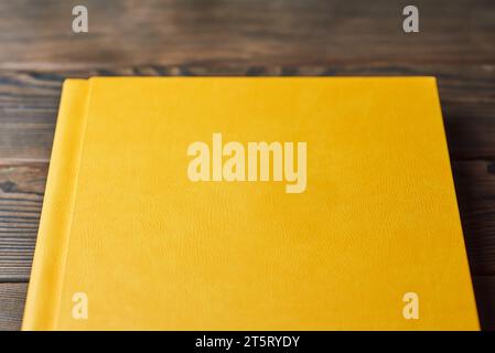 Book with yellow textured hardcover isolated on a brown wooden background. Perspective view, close-up, cropped. Layout with blank cover. Concept of re Stock Photo