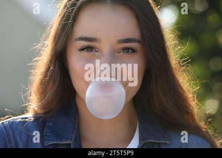 Beautiful young woman blowing bubble gum outdoors Stock Photo