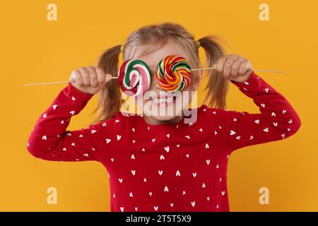 Happy girl covering eyes with lollipops on orange background Stock Photo