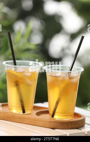Plastic cups of tasty iced tea with lemon on white wooden table against blurred background Stock Photo