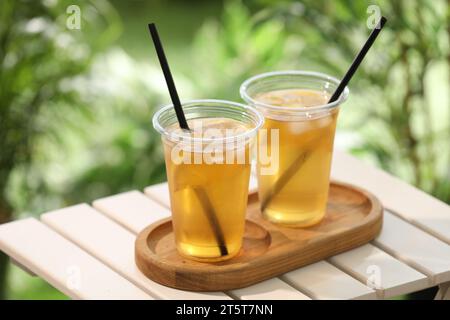 Plastic cups of tasty iced tea with lemon on white wooden table against blurred background Stock Photo
