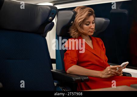 Young beautiful lady traveling by the train sitting near the window using mobile smartphone. 5g online mobile technology in transport trip journey. Co Stock Photo