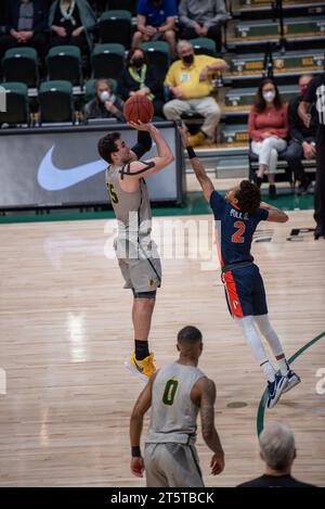 College basketball player taking a contested jump shot during NCAA game ...