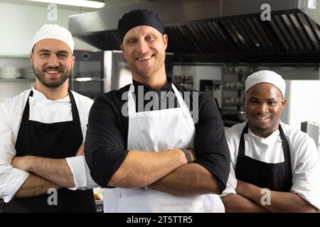 Three happy diverse male chefs standing with arms crossed in restaurant kitchen Stock Photo