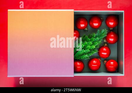 Small pine tree and red baubles in the box that have space for text on red background. Christmas holiday concept. Stock Photo