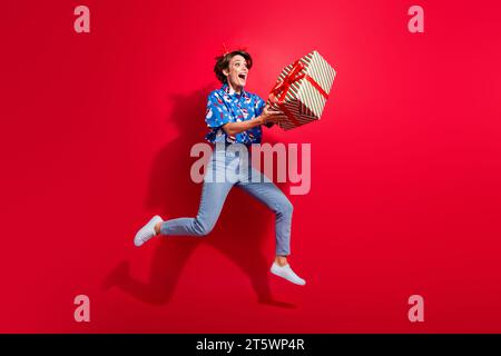 Full size photo of body young girlfriend running in air happy positive hold big surprise gift box noel eve isolated on red color background Stock Photo