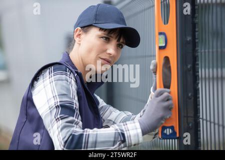 woman building metal fence checking regularly with a spirit level Stock Photo
