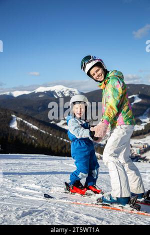 preschool boy and teenage girl, brother sister, are relaxing at ski resort, joyfully standing on skis at top of mountain slope. Winter active entertai Stock Photo