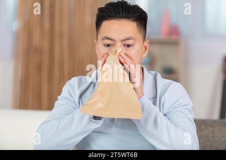 man with panic attack breathing in paper bag at home Stock Photo