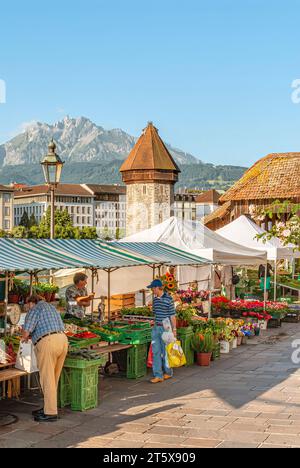 Market stands in front of the Chapel Bridge (Kapellbrücke) at the waterfront of the River Reuss in Lucerne, Switzerland. Stock Photo