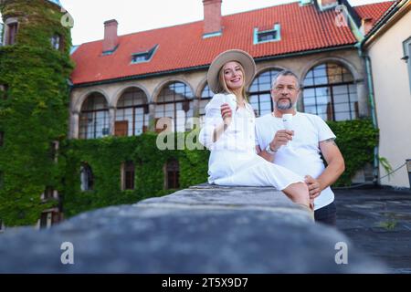 Portrait of cheerful middle-aged lovers are embracing and laughing. They are standing outside in elegant clothing and holding glasses of champagne. Stock Photo