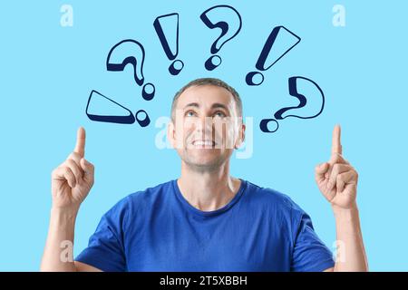 Portrait of mature man pointing at question and exclamation marks on light blue background Stock Photo