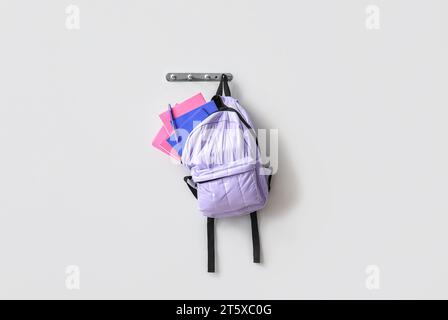 School backpack with stationery hanging on light wall Stock Photo