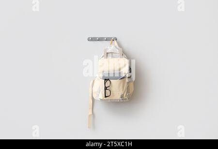 School backpack with stationery and eyeglasses hanging on light wall Stock Photo
