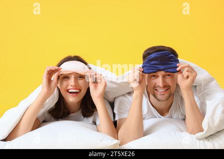 Young couple with blanket and pillows lying on yellow background Stock Photo