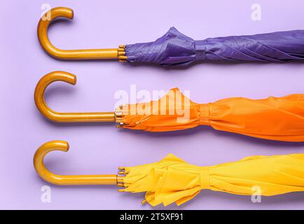 Different stylish umbrellas on lilac background Stock Photo