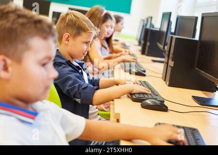 Smiling elementary schoolkid using computer with friends in class Stock Photo