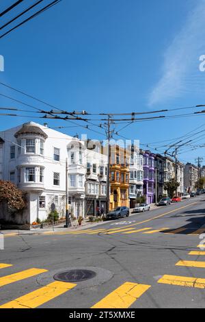 Castro Street, San Francisco, California, USA - April 23, 2023: Colorful houses on steep street with parked cars on asphalt road with yellow marks and Stock Photo