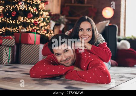 Closeup photo of cute beautiful couple lying on carpet woman piggyback man posing for camera indoors interior christmas concept background Stock Photo