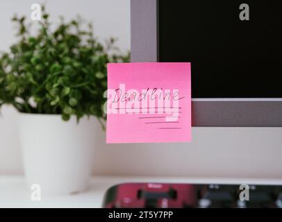 A pink paper notes with the reminder Deadline on it sticked on to a monitor at an office workplace. Stock Photo