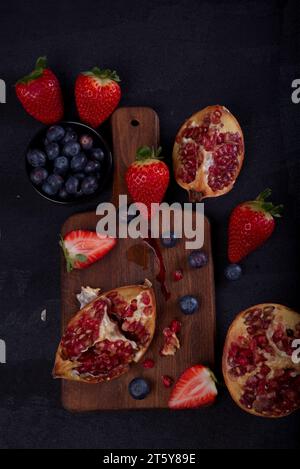 Strawberries, blueberries and pomegranates exposed on a wooden board in dark background. Stock Photo
