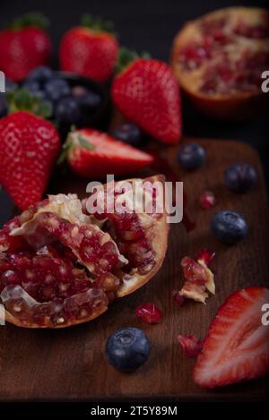 Strawberries, blueberries and pomegranates exposed on a wooden board in dark background. Stock Photo