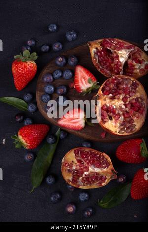 Strawberries, blueberries and pomegranates exposed on a wooden board in dark background. Stock Photo