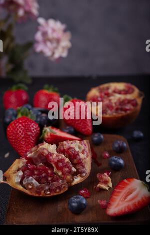 Strawberries, blueberries and pomegranates exposed on a wooden board in dark background. Stock Photo