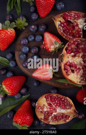 Strawberries, blueberries and pomegranates exposed on a wooden board in dark background. Stock Photo