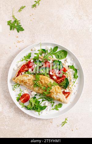 Omelette stuffed with tomato, broccoli, feta cheese and fresh green leaves of arugula and spinach. Healthy diet food, breakfast. Top view Stock Photo