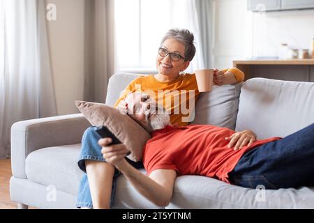 Retirement Pastime. Smiling Elderly Spouses Relaxing On Couch At Home Stock Photo