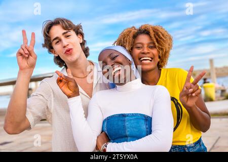 Portrait of three friends gesturing peace while smiling in an urban space Stock Photo