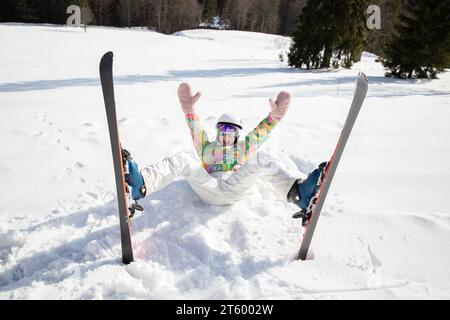 young woman or teenage girl in good mood while skiing fell and lies cheerfully in the snow. enjoying the moment, digital detox, positive thinking. Int Stock Photo