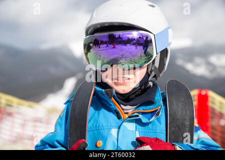 portrait of a boy's face in a helmet, ski goggles at a ski resort against the backdrop of a mountain landscape. Winter activities for children. cold s Stock Photo