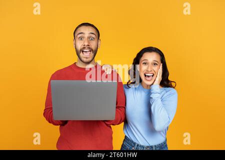 Shocked young couple using modern laptop on yellow Stock Photo