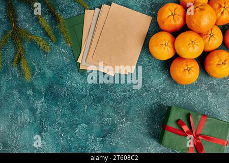 fresh tangerines and multicolored envelopes near pine branches on blue texture, Christmas still life Stock Photo