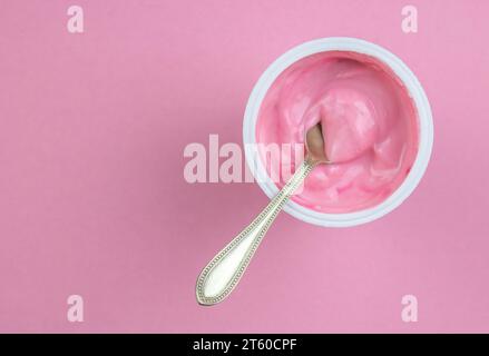 Strawberry pink yogurt in small plastic cup with little spoon isolated on pink background with copy space Stock Photo