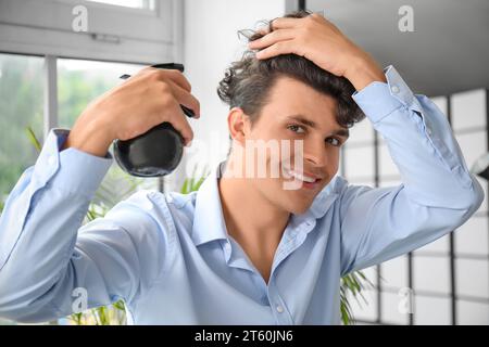 Handsome young man applying hair spray on his curly hair in hallway Stock Photo