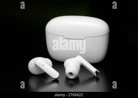 Wireless headphones in white case isolated on black background. Stock Photo