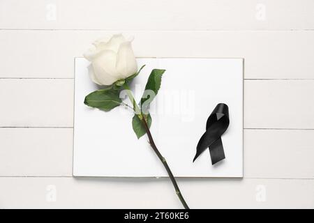 Rose with black ribbon and blank open notebook on white wooden background Stock Photo