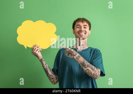 Happy young man pointing at blank speech bubble on green background Stock Photo