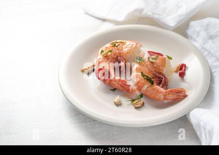 Fried tiger prawns or shrimps with garlic, herbs and red chili pepper served on a white plate, spicy gourmet seafood dish from fresh crustaceans, copy Stock Photo