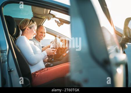 Happy smiling two young adulds couple using smartphone navigation inside car during auto jorney.They are laughing during road trip. Family, couples re Stock Photo