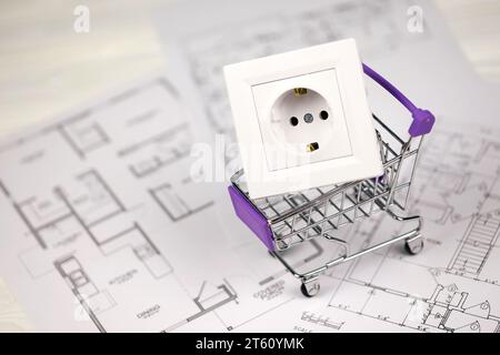European standard EU outlet in small shopping cart on blueprints of residential house plan close up. Concept of shopping and electricity devices Stock Photo