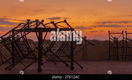 Metal chairs out on a patio as the sky turns golden as the sunsets Stock Photo
