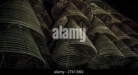 Multiple large yellow incense coils hanging in stacks from the Ceiling in a Chinese shrine. Large Bell Shaped Spiral Incense Coils, Focus and blur. Stock Photo