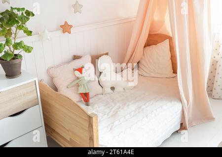 large bright bedroom with white walls and a large bed with a white knitted bedspread. near the bed there is a small wicker cradle with a toy Stock Photo